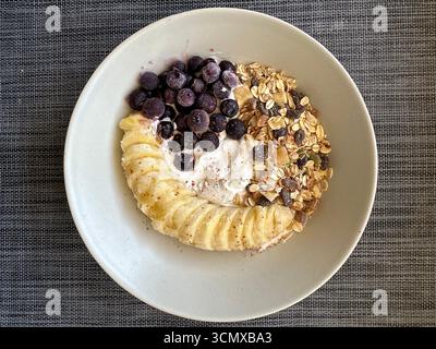 Hafer mit Bananenscheiben, gefrorenen Heidelbeeren, Schokoladenchips und Joghurt. Natürlich süß, erfrischend und ideal für ein schnelles, nahrhaftes Frühstück Stockfoto