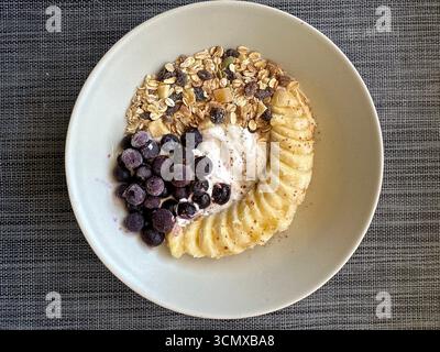 Hafer mit Bananenscheiben, gefrorenen Heidelbeeren, Schokoladenchips und Joghurt. Natürlich süß, erfrischend und ideal für ein schnelles, nahrhaftes Frühstück Stockfoto