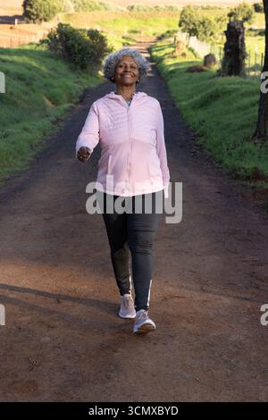 afroamerikanische Seniorin, die in Jacke und Leggings an Zaunpfosten vorbeiläuft Stockfoto