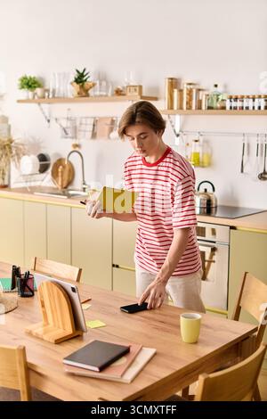 In einer stilvollen Wohnung studiert ein junger Mann online, während er Notizen und ein Telefon ausbalanciert. Stockfoto