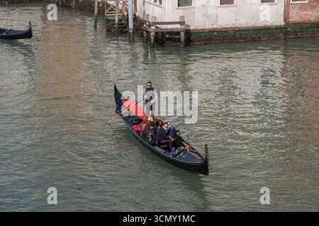 Gondelbahn mit Gruppe von Menschen und Gondoliere im Canal Grande in Venedig, Italien. Traditionelles venezianisches Boot mit Touristen Familie auf Besichtigungstour. Stockfoto