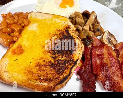 Warmes Frühstück mit dickem Toast, gebackenen Bohnen mit Würstchen, Speck, Pilzen und Spiegelei Stockfoto