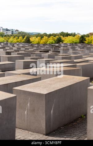 Berlin, Deutschland - 1. September 2025: In Berlin spazieren Besucher durch große graue Steinblöcke am Holocaust-Denkmal, umgeben von lebendigen Bäumen und Stockfoto