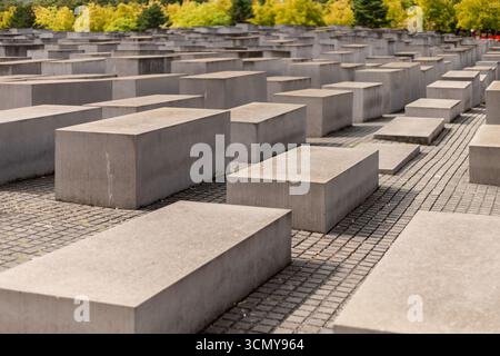 Berlin, Deutschland - 1. September 2025: Besucher spazieren durch die Betonplatten des Holocaust-Gedenkwerks in Berlin, umgeben von Bäumen. Der klare Himmel en Stockfoto