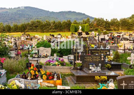 Milowka, Polen, 08.07.2021. Friedhof mit traditionellen Granitgräbern, dekoriert mit bunten künstlichen Blumen und Kerzen in den Beskid Mountains. Stockfoto