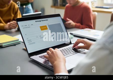 Junge Erwachsene Frau mit Laptop mit KI-Bildgenerator-Schnittstelle auf dem Bildschirm, sitzt am Schreibtisch in einem modernen Büro, während zwei Kollegen, junge Erwachsene, im Hintergrund arbeiten Stockfoto