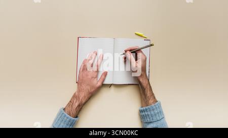 Top-down-Ansicht eines Mannes, der Notizen in einem Bullet Journal macht. Kreatives Schreiben, Planen und Leere-Page-Syndrom auf einem isolierten Modell. POV isoliert. Stockfoto