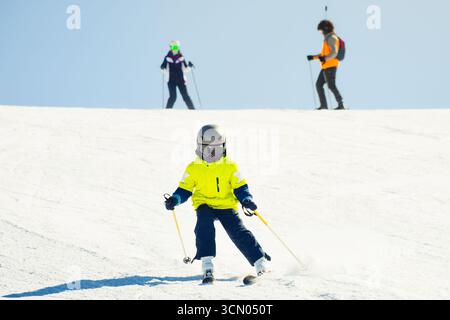 Boy Child Skier in knallgrüner Jacke lernt auf schneebedeckten Pisten im Bergskigebiet im Familienurlaub im Winterurlaub in den hochalpen Ski fahren Stockfoto