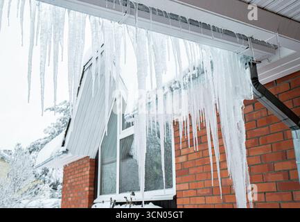 Große Eiszapfen hängen im Winter an der Regenrinne eines Privathauses. Gefahr des Bruchs und der Beschädigung der Regenrinnen. Stockfoto