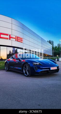 Vilnius, Litauen - 01.05.2024 - Blauer Luxus Porsche Taycan, vollelektrisch vor dem Händlerbetrieb bei Sonnenuntergang geparkt Stockfoto