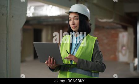 Asiatische Koreanisch Chinesische japanische Frau hält Laptop Tippen Zählen Berechnung Builder in Hutarbeiter weibliche Mädchen Inspektor Ingenieur mit Stockfoto