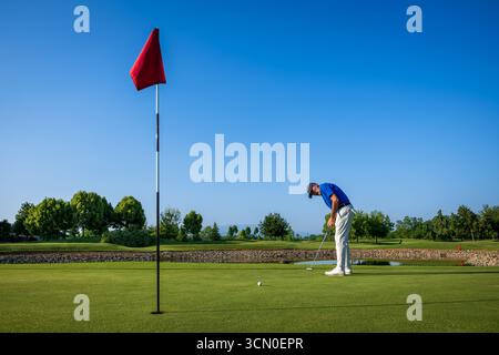 Golfer, die sich darauf konzentrieren, den Ball an einem sonnigen Tag auf einem wunderschönen Golfplatz ins Loch zu legen Stockfoto