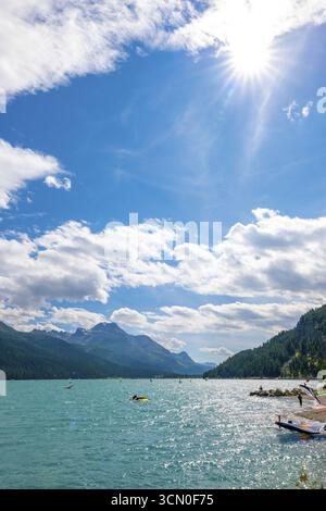 Windsurfen und Wingsurfen auf dem Alpensee Silvaplana an einem sonnigen Sommertag mit Bergblick in den Schweizer Alpen und Sonnenstrahl in Silvaplana, Maloja, Gr Stockfoto