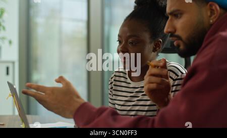 Multiethnische Kollegen eines informellen Unternehmensgründers im Büro mit Laptop afroamerikanische Geschäftsfrau sprechender indischer Geschäftsmann Mentor hilft Stockfoto