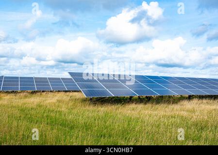 Reihen von Solarpaneelen in einer Solarlandschaft unter einem hellblauen Himmel mit verstreuten Wolken. Szene für erneuerbare Energien, die saubere Technologie und e zeigt Stockfoto