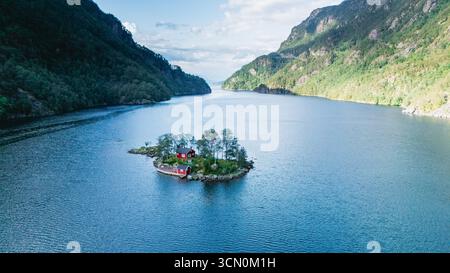 Lovrafjorden bietet einen atemberaubenden Blick auf eine bezaubernde rote Hütte auf einer winzigen Insel, umgeben von ruhigem Wasser und üppigen Bergen. Stockfoto