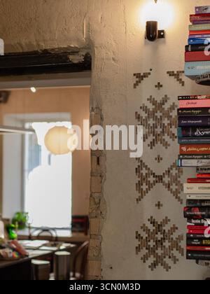 Bücher stapelbar auf Wandregalen mit Vintage-Lampe in stilvollem Café-Interieur, rustikale Atmosphäre, Kiew, Ukraine. Stockfoto