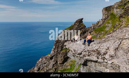 Der atemberaubende Aussichtspunkt auf dem Matind Mountain zeigt dramatische Klippen und den endlosen Ozean dahinter. Zwei Abenteurer genießen die ruhige Schönheit an einem sonnigen Tag und fangen das Wesen der Landschaft Norways ein. Stockfoto