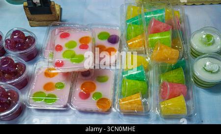 Gemischtes thailändisches Gelee-Dessert mit Kokosmilch, farbenfrohen geometrischen und runden Formen in Plastiktabletts, die lebendige asiatische süße Traditionen widerspiegeln. Stockfoto