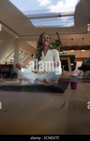 Eine ältere ältere Frau sitzt zu Hause in ihrem Wohnzimmer und macht Yoga-Übungen, um sich zu entspannen und fit und aktiv zu bleiben. Stockfoto