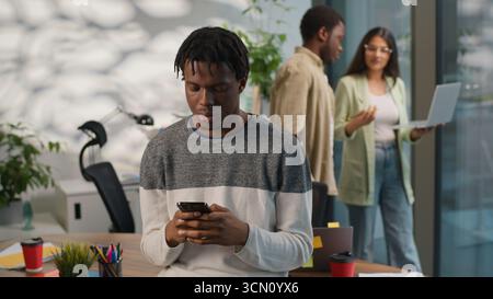 Afroamerikanischer konzentrierter Mann informeller Business Startup-Arbeiter männlicher Kerl Geschäftsmann mit Handy-abhängigem Smartphone chatten zwei multirassische Stockfoto