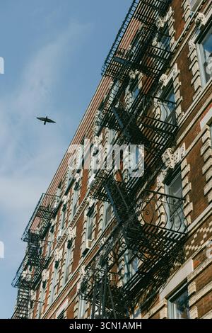 In einem Gebäude aus rotem Backstein gibt es mehrere Fluchtwege, während ein Vogel über dem Himmel gegen einen klaren blauen Himmel fliegt. Stockfoto