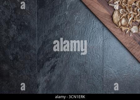 Getrocknete Austernpilze auf Holzbrett oben auf dunklem Schiefer, Studiostillleben. Der Rest des Rahmens lässt freien Platz für Text oder Design Stockfoto