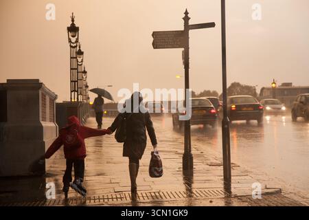 LONDON, GROSSBRITANNIEN. 19. OKTOBER 2010. Eine Mutter hält die Hand ihres Kindes, während sie bei Sonnenuntergang eine verregnete Londoner Brücke überquert, um flüchtige Kindheitserinnerungen festzuhalten Stockfoto