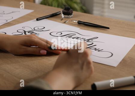 Kalligraphie. Frau mit Pinsel schreibt Worte Danke auf Blatt Papier am Holztisch, Nahaufnahme Stockfoto