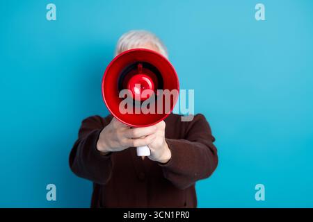 Energische Frau, die ein Megaphon auf einem leuchtend blauen Hintergrund verwendet, um Kommunikation und Fürsprache auszudrücken Stockfoto