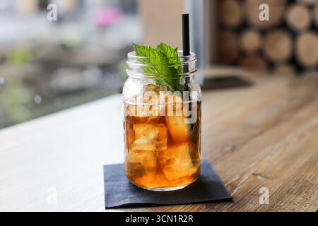 Erfrischender Eistee mit Minzblättern. Kaltes Getränk in Glasgefäß mit Strohhalm. Sommergetränk auf Holztisch. Gesunde Erfrischung Konzept Nahaufnahme. Stockfoto