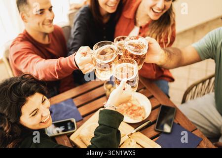 Aus einem hohen Winkel stoßen eine Gruppe glücklicher Freunde ihre Bierbecher in einem Toast über einem Holztisch mit Pizza an, um einen Moment der Zweisamkeit zu feiern. Stockfoto