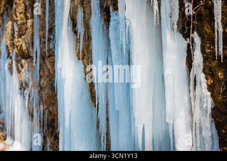 Gefrorener Wasserfall mit langen Eiszapfen auf einer felsigen Klippe an sonnigen Wintertagen. Stockfoto