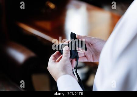 Der Bräutigam hält während der Vorbereitungen am Hochzeitmorgen eine elegante schwarze Schleife in den Händen Stockfoto