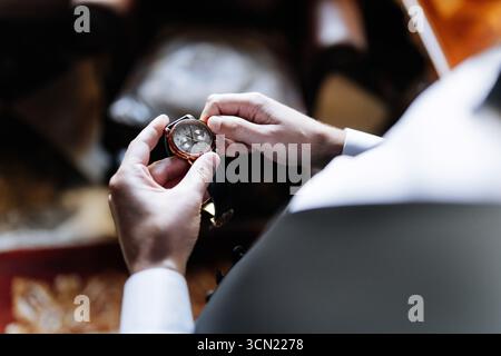 Eleganter Bräutigam, der die luxuriöse Armbanduhr vor der Hochzeitszeremonie anpasst, Nahaufnahme der Hände Stockfoto