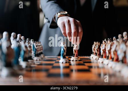 Mann im Anzug, der Schach mit kunstvollen Stücken auf luxuriösem Holzbrett spielt Stockfoto