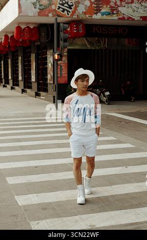 Ho-Chi-Minh-Stadt, Vietnam – 30. April 2015: Straßenportrait eines hübschen jungen asiatischen Mannes mit Händen in Taschen, die Fedora-Hut tragen. Das Gebäude ist mit chinesischen Laternen dekoriert Stockfoto