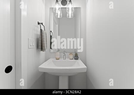 Kleines Badezimmer mit weißem Waschbecken und Spiegel. Der Spiegel befindet sich über dem Waschbecken und ist mit einem Licht darüber beleuchtet. An der Wand hängen zwei Handtücher Stockfoto