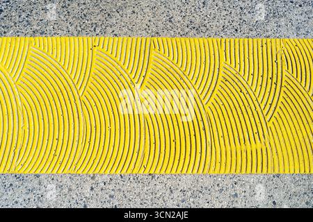 Nahaufnahme einer strukturierten gelben Linie auf einer Betonoberfläche mit wellenartigen Mustern Stockfoto