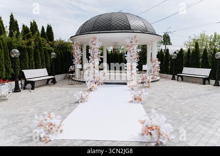 Elegante Hochzeitszeremonie mit Blumenbogen im luxuriösen Garten im Freien Stockfoto