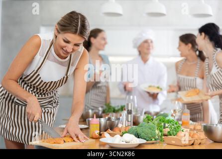 Mädchen in der Kochschule schneidet Hühnchen und bereitet kalorienarmes Mittagessen zu Stockfoto