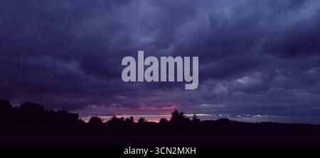 Ein dramatischer Sonnenuntergang, der sich unter bewölktem Himmel entfaltet und die natürliche Schönheit um uns herum einfängt Stockfoto