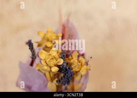 Getrockneter Blumenstrauß mit gelben und violetten Blüten. Eine Nahaufnahme eines Straußes getrockneter Blumen, die in lila Papier gewickelt sind und Gelb und Lila zeigen Stockfoto