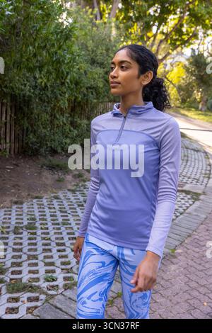 Indische Frau, die in Sportkleidung auf Parkpfeilern neben dem Holzzaun läuft Stockfoto