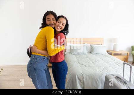 Vielfältige Mutter und Tochter im Teenageralter in einem modernen Schlafzimmer mit silbernem Koffer und Reisepass Stockfoto
