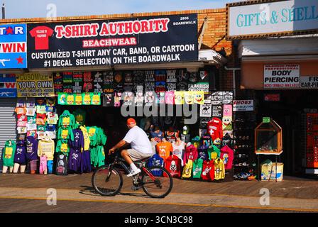 Ein erwachsener Mann fährt mit dem Fahrrad an einem T-Shirt-Shop auf dem Boardwalk in Wildwood, New Jersey Stockfoto