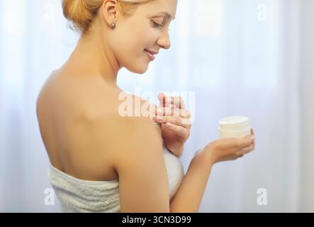 Nahaufnahme einer jungen Frau der 30er Jahre, die Feuchtigkeitscreme auf ihre Haut aufträgt Stockfoto