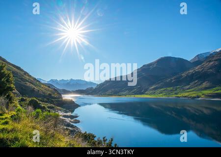 Küste am Lake Wanaka an einem schönen sonnigen Tag mit einem Sonnenschein am wolkenlosen Himmel Stockfoto