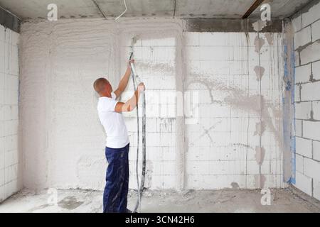 Baufirma, die Wände mit einer Putzpumpenmaschine im Innenbereich verputzt. Stockfoto