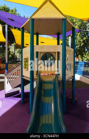 Farbenfrohe Spielplatzrutsche mit schattigen Strukturen im Park. Stockfoto